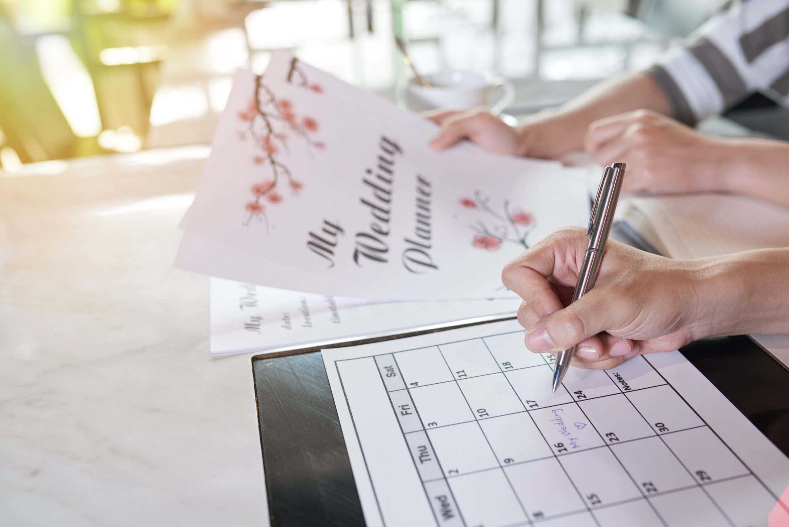 Young couple planning wedding day together and taking necessary notes in calendar while sitting at home, close-up shot